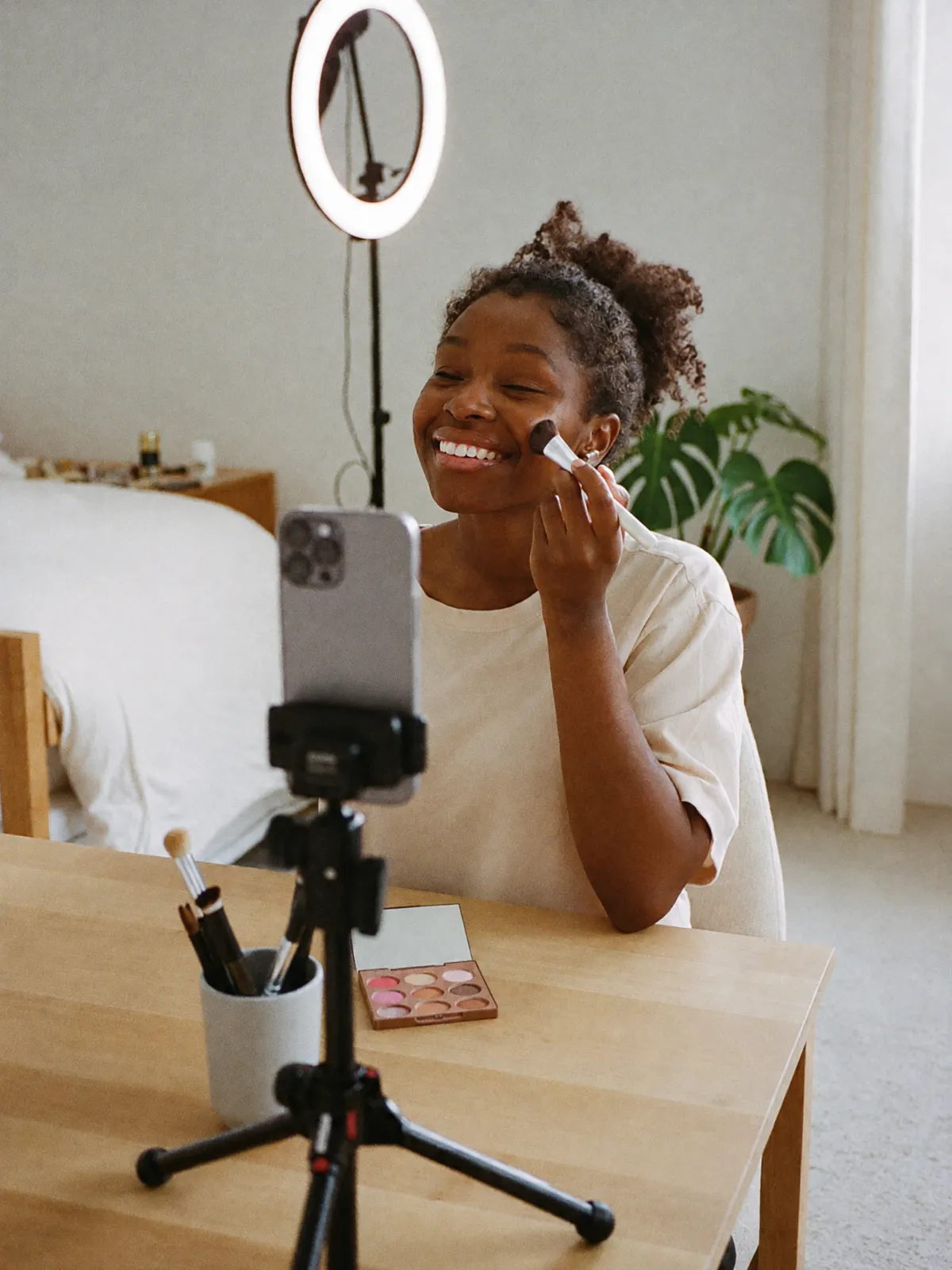 A woman doing her make-up at her vanity, filming herself with her phone on a tripod