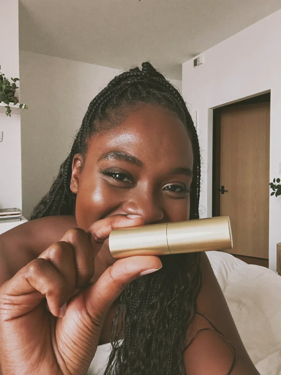 A woman laughing, holding a lipstick up to her phone camera