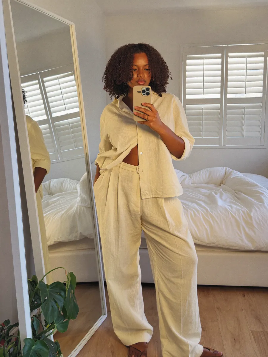 A woman taking a mirror selfie of her outfit next to her bed