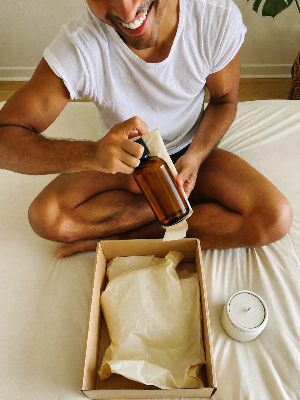 A man unboxing a skincare bottle on his bed, seen from above